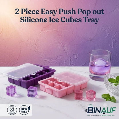 Two silicone ice cube trays in purple and pink are displayed on a white marble surface with ice cubes and a glass of purple liquid. The background is a textured purple wall with promotional text at the top and the BINAUF logo at the bottom right.